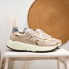 Sneaker in rosegoud op een houten kruk